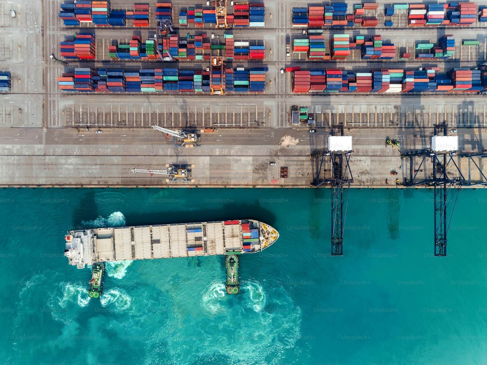 Aerial view of a cargo ship guided by tugboats into a container terminal
